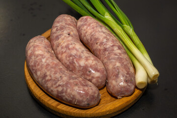 Meat sausages with garlic and green onions, prepared for grill, on a wooden board. Raw sausages for...
