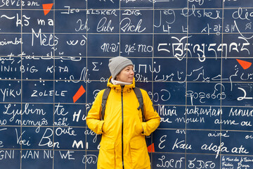 Paris, France - February 28, 2025: A female tourist stands smiling in front of the Wall of Love in...