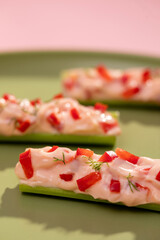 Stuffed Celery with Cheese and Red Peppers on Colorful Background – Healthy Vegetarian Snack. Flat lay of stuffed celery sticks, boats, modern plant-based cuisine