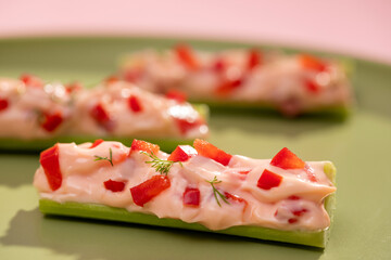 Stuffed Celery with Cheese and Red Peppers on Colorful Background – Healthy Vegetarian Snack. Flat lay of stuffed celery sticks, boats, modern plant-based cuisine