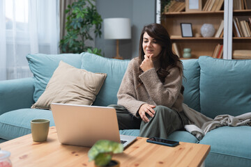 Young woman attending online therapy session from her living room, expressing emotion while talking...