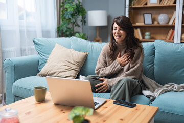 Young woman attending online therapy session from her living room, expressing emotion while talking...