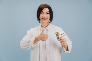 Middle aged woman recommending pills with thumbs up, promoting healthcare and pharmaceuticals