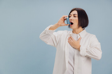 Mature Woman Using Inhaler for Asthma Attack on Blue Background