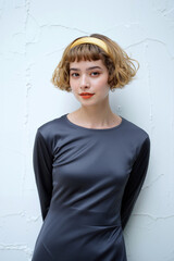 A young woman poses elegantly with her hands behind her back, showcasing a chic outfit and bright lipstick, set against a light textured wall. Generative AI.