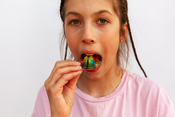 Young girl in pink t-shirt putting orthodontic plate on teeth with uneven teeth, malocclusion on white background. Concept orthodontic treatment