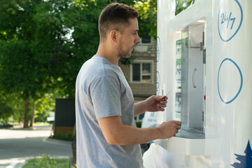 Adult filling reusable bottle with filtered water at urban water vending machine. Eco friendly and...