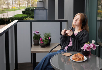 beautiful teenager girl in headphones with cup of tea on balcony