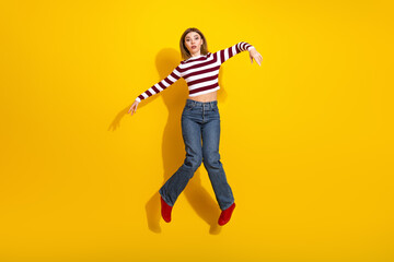 Playful young woman in striped outfit posing casually against a bright yellow background, expressing confidence and stylish charm