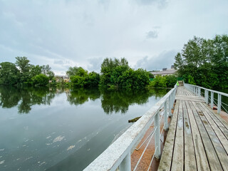 There is a beautiful wooden bridge that gracefully spans over a peaceful lake, framed by lush green...