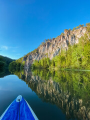 A vibrant and colorful kayak drifts peacefully across the tranquil river waters, while a magnificent mountain looms majestically in the background, forming a breathtaking natural scene