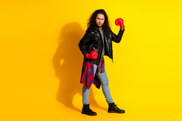 Confident young man in a leather jacket and boxing gloves posing against a vibrant yellow...
