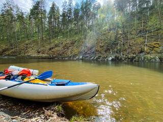 A vibrant and colorful kayak is parked on the sandy shore of a serene and tranquil river, eagerly awaiting a day filled with adventure and exciting activities on the water ahead of it