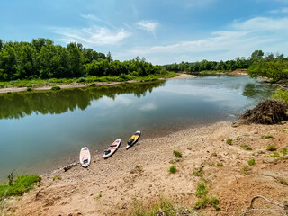 Three colorful kayaks are resting on the sandy shore of a beautiful river, waiting for adventurous paddlers to take them out onto the water for an exciting journey ahead