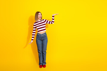 Young woman in striped pullover gesturing against vibrant yellow background showcasing trendy...