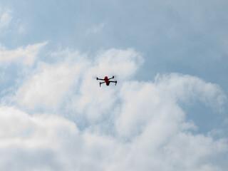 A red drone is flying in the sky above a cloudy day