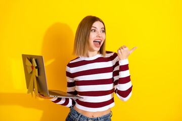 Smiling young woman holding a laptop with a gift bow, wearing a striped top, gesturing cheerfully...