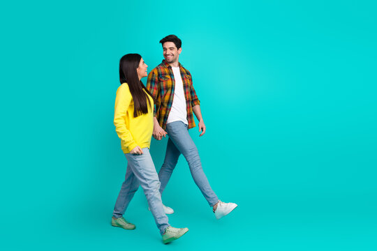 Young couple walking together against a teal backdrop, holding hands and smiling, embodies love, friendship, and happiness