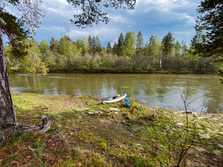 A bright, colorful kayak is patiently resting on the sandy shore of a serene river, surrounded by lush greenery and vibrant trees, embodying the essence of natures beauty and tranquility