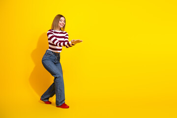 Portrait of a stylish young woman presenting and gesturing isolated against a vibrant yellow background