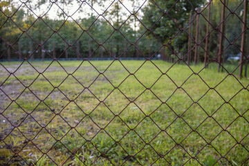 Fence with a chain link pattern is in a field. The fence is empty and the grass is green
