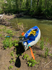 A kayak is resting calmly on the ground beside a flowing river, waiting for its next adventure on the water. This watercraft is perfect for exploring waterways in a recreational way