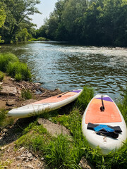 On a tranquil riverbank, two vibrant and colorful paddle boards are perfectly positioned, eagerly awaiting the fun activities and exhilarating water sports adventures that lie ahead