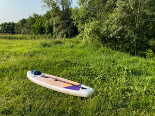 A paddle board is placed on top of a vast and lush green field filled with vibrant grass and colorful wildflowers, creating a picturesque scene of adventure and outdoor fun