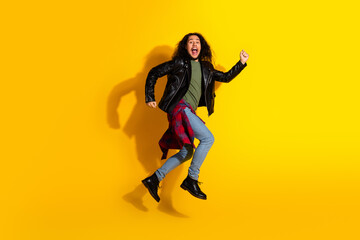 Young man with long hair and stylish leather jacket jumps against bright yellow background showcasing joy and energy