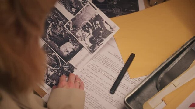 Female detective or government agency analyst and spy reviewing various classified papers and top secret information reports and folders on office desk. Sensitive text revealed and exposed to public