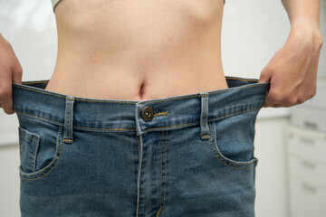 Young Asian woman losing weight wearing loose pants in oversize jeans.