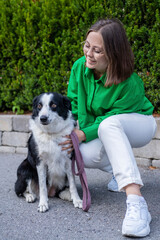 A girl in white trousers, green shirt, and sunglasses embraces her dog amid Norwegian greenery — a moment of love, trust, and natural beauty.