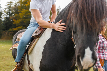 A man wearing jeans and a white t-shirt sits on a Pinto Horse, gently touching its neck in a green...