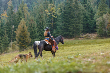 Skilled cowgirl on horseback, riding a beautiful black horse through a mountain wilderness