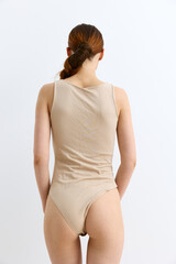 Obraz premium woman in beige bodysuit standing with back turned, red hair tied, minimalistic style, plain white background, natural light, skin exposure