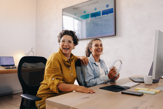 Two female colleagues laughing together in a friendly office setting - Powered by Adobe