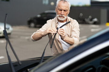 Senior man replacing windshield wipers on car in parking lot