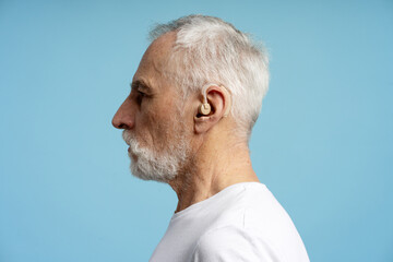Senior man wearing hearing aid showing profile on blue background
