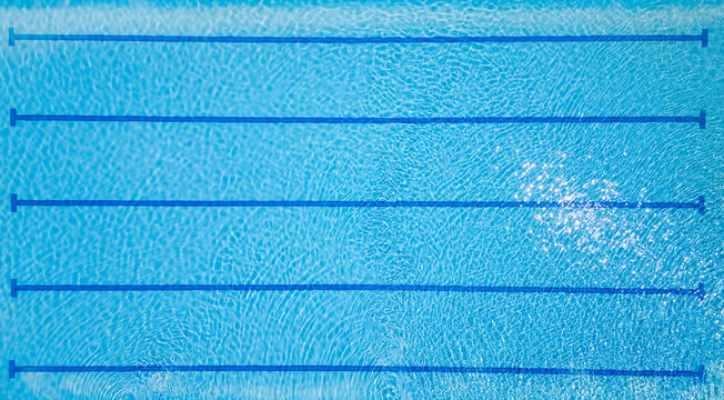 Top-down view of an empty swimming pool with lane dividers and clear blue water. Sunny reflections and clean geometry make it perfect for fitness, sports, and summer themes