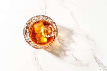 Whiskey with ice cube in the glass at white table.