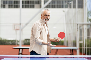 Senior man playing ping pong outdoors, serving the ball with paddle