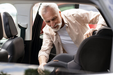 Grandfather installing child safety seat in car for grandchild