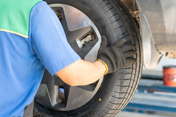 Action from back of a technician man is installing a car wheel after new tire replacement. Working person scene, selective focus.