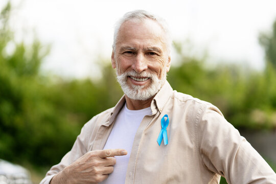 Senior man showing blue ribbon for prostate cancer awareness month