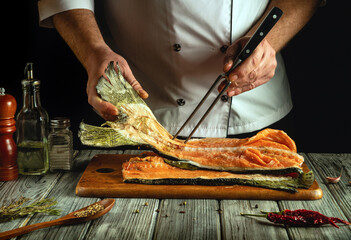 A chef skillfully handles a large fillet of salted fish on a cutting board. Various spices and...