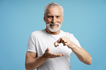 Senior smiling man showing hearing aid while smiling on blue background