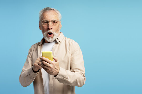 Shocked senior man reading unexpected news on smartphone on blue background