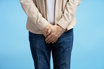 Senior man experiencing discomfort holding groin area on blue background