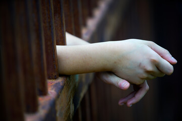 Hand Reaching Through Rusted Bars in a Dimly Lit Setting