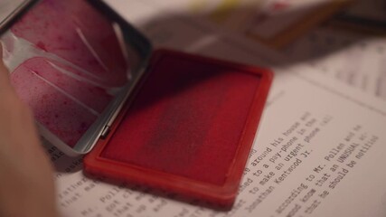 Close up on red ink pad as hand press stamp to mark document as classified. Government official or agent labeling papers for censorship and archive. Sensitive information to be kept secret and hidden - Powered by Adobe